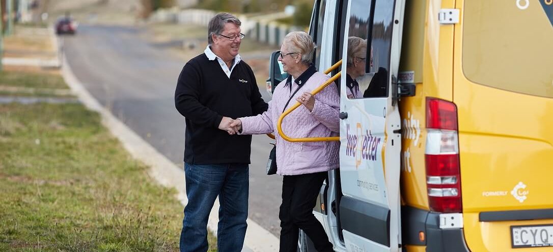 Volunteer helping an older lady step off a LiveBetter bus