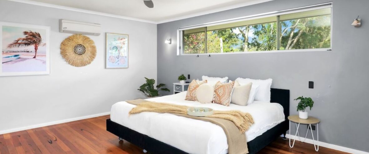 A stylish bedroom that includes a bed, a ceiling fan, and a beautiful full length window that lets lots of natural light in.