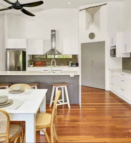 Cosy kitchen featuring a wooden dining table surrounded by chairs, with cabinetry and countertops visible. The floor is covered in laminate and wood, and a ceiling fan hangs overhead. A vase adds a decorative touch to the space.