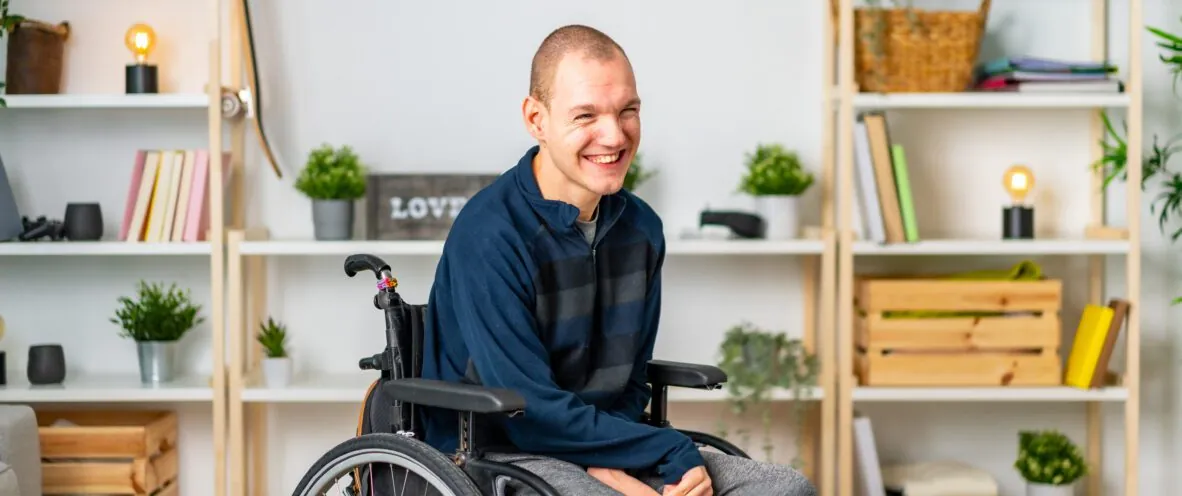 Smiling man in a wheelchair sitting in a bright, cosy living room.
